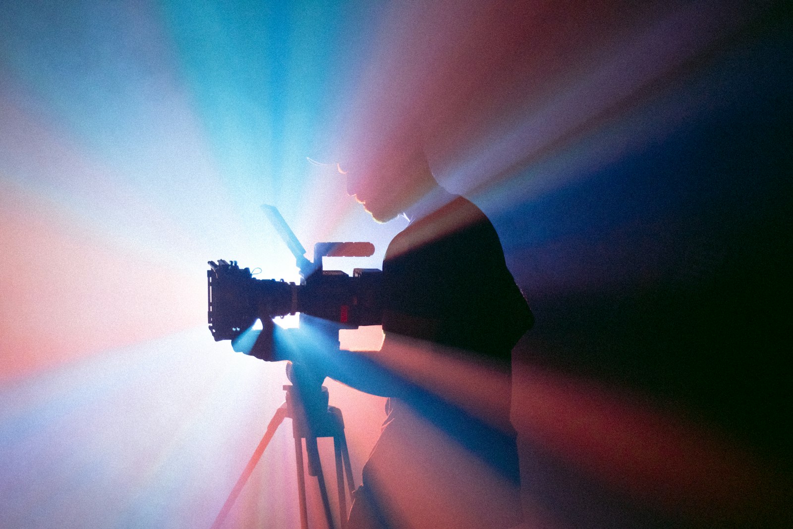 A camera operator silhouetted behind a cinema camera in streaked stage light.
