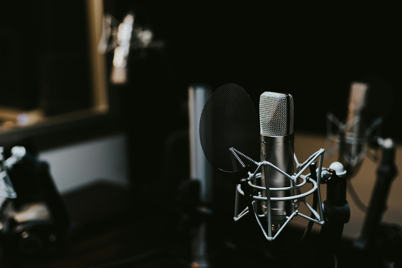 A condenser microphone on a shock mount in a dimly lit recording studio.