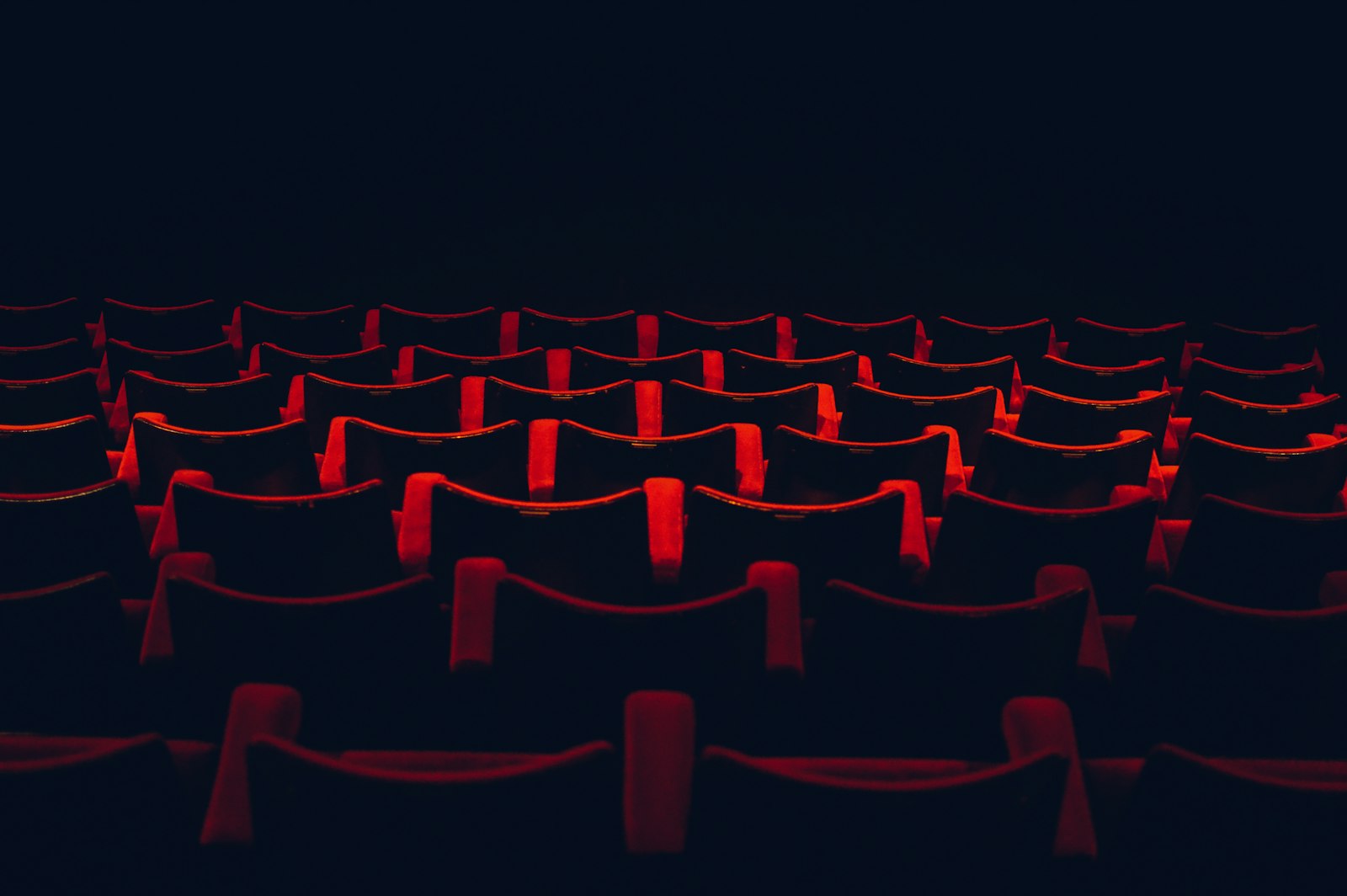 Rows of empty theatre seats in deep shadow, washed by low red light.
