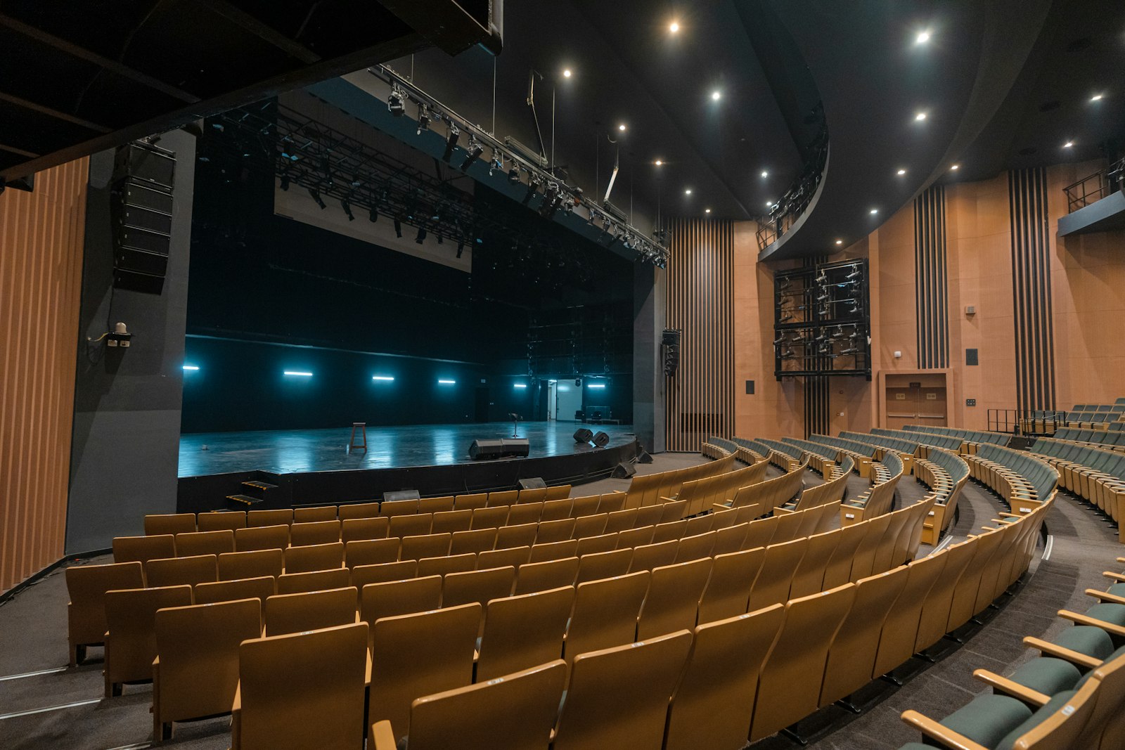 An empty auditorium seen from the back rows, its stage lit by teal light bars.